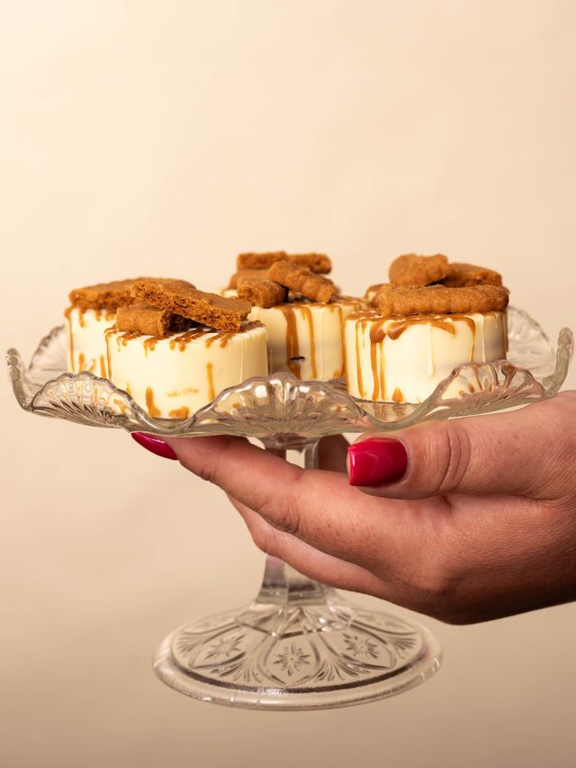 En hand som räcker fram ett glasfat med cheesecakebitar toppade med biscoff.