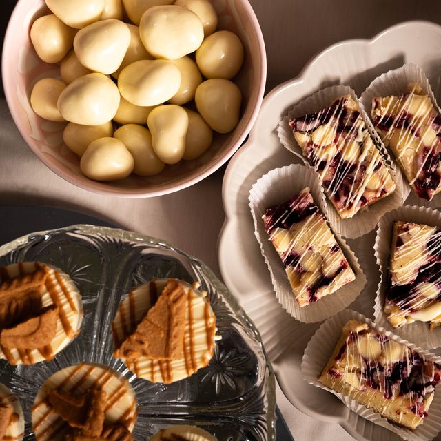 Skål med vit choklad bredvid fat med cheesecakebitar och kakor.