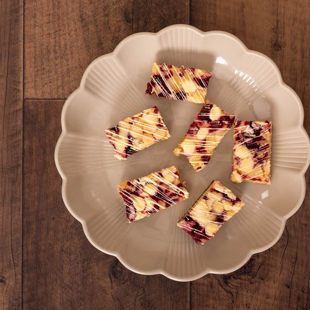 Vitt fat ovanifrån med cheesecakebitar dragna med bärsås, på mörkt trä.